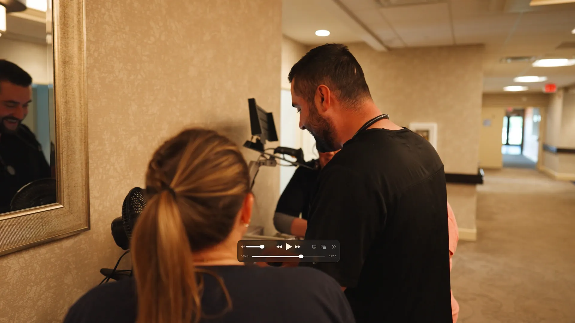 Two staff reviewing a wall-mounted monitor together in a hallway
